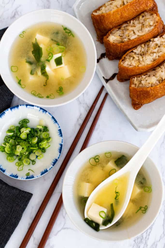 Miso soup with tofu and wakame seaweed served alongside inari sushi and sliced green onions