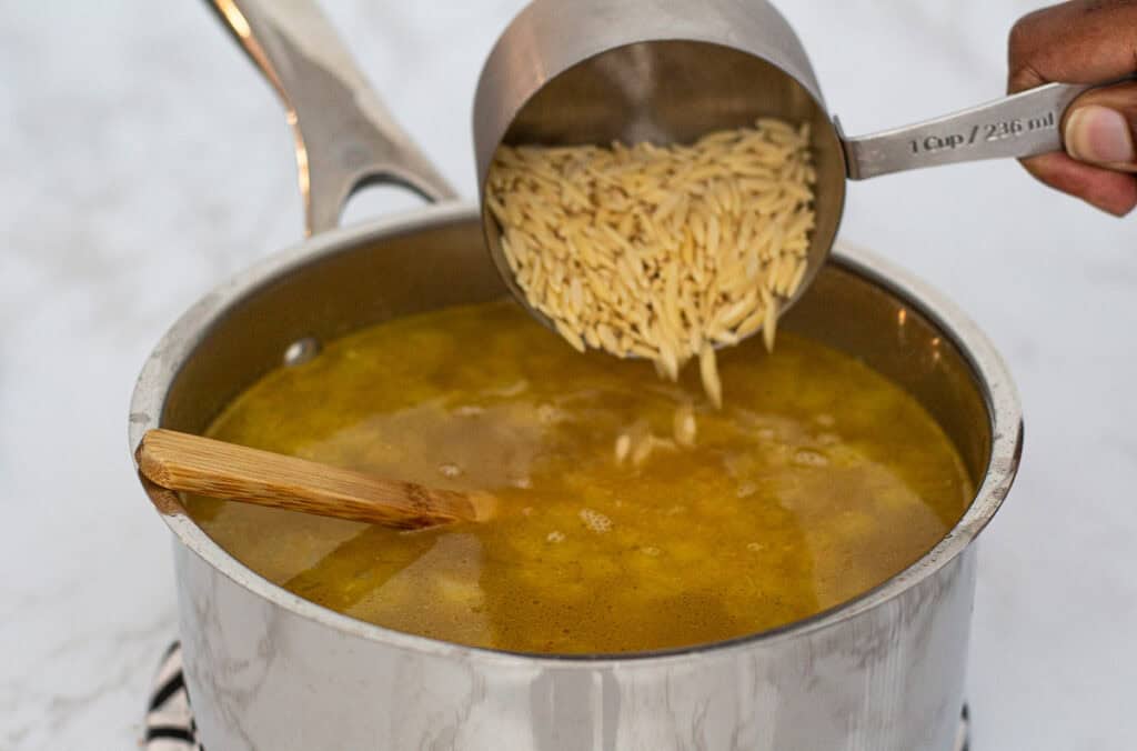 Dry orzo poured into simmering broth.