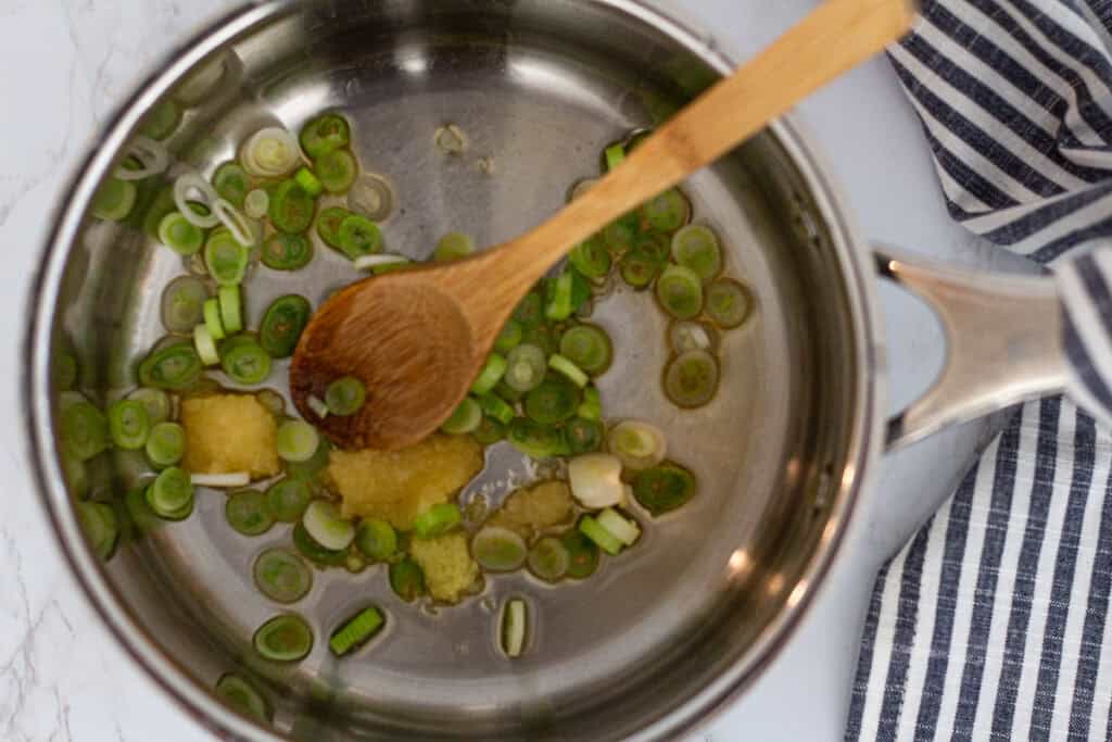Garlic, ginger, and green onions sautéing in a pot to start the base for dumpling noodle soup.