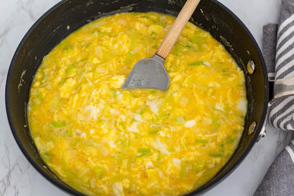 Egg mixture partially set with leeks in a skillet before baking.