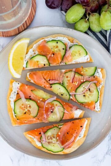 Smoked salmon flatbread topped with cucumber, red onion, and everything bagel seasoning, sliced and ready to serve.
