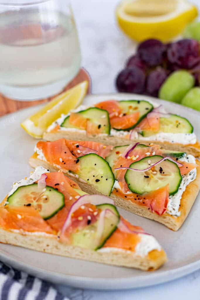 Close-up of smoked salmon flatbread with cream cheese, cucumber, and lemon wedge on the side.