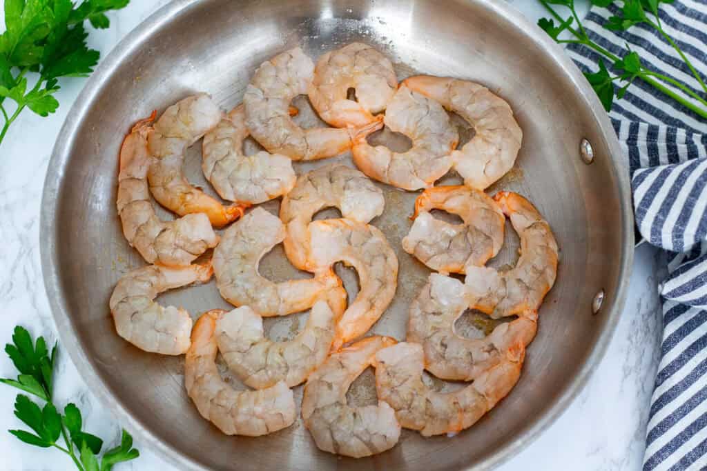 Raw shrimp arranged in a single layer and searing in a stainless steel skillet.