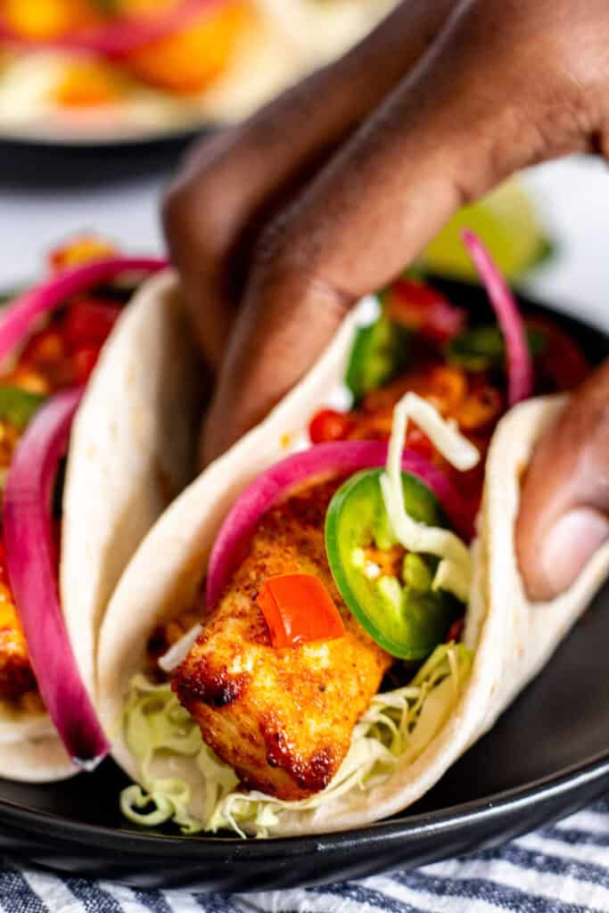 Blackened fish taco with mahi mahi, cabbage, pickled red onions, jalapeño, and corn, held in a warm tortilla.