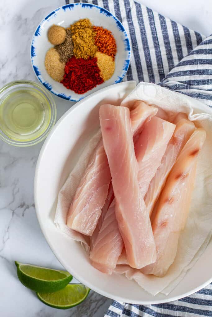 Raw mahi mahi fillets with homemade blackening spice mix and lime, prepped for blackened fish tacos.