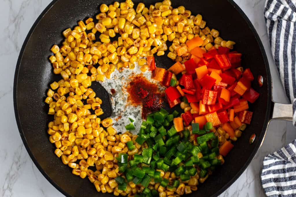 Overhead view of sautéed corn with chopped bell peppers and seasoning added in a skillet