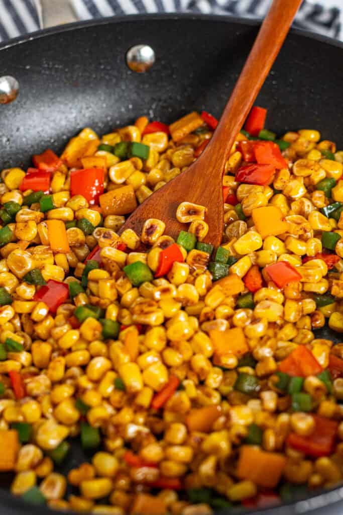 Close-up of sautéed corn with bell peppers being stirred in a skillet