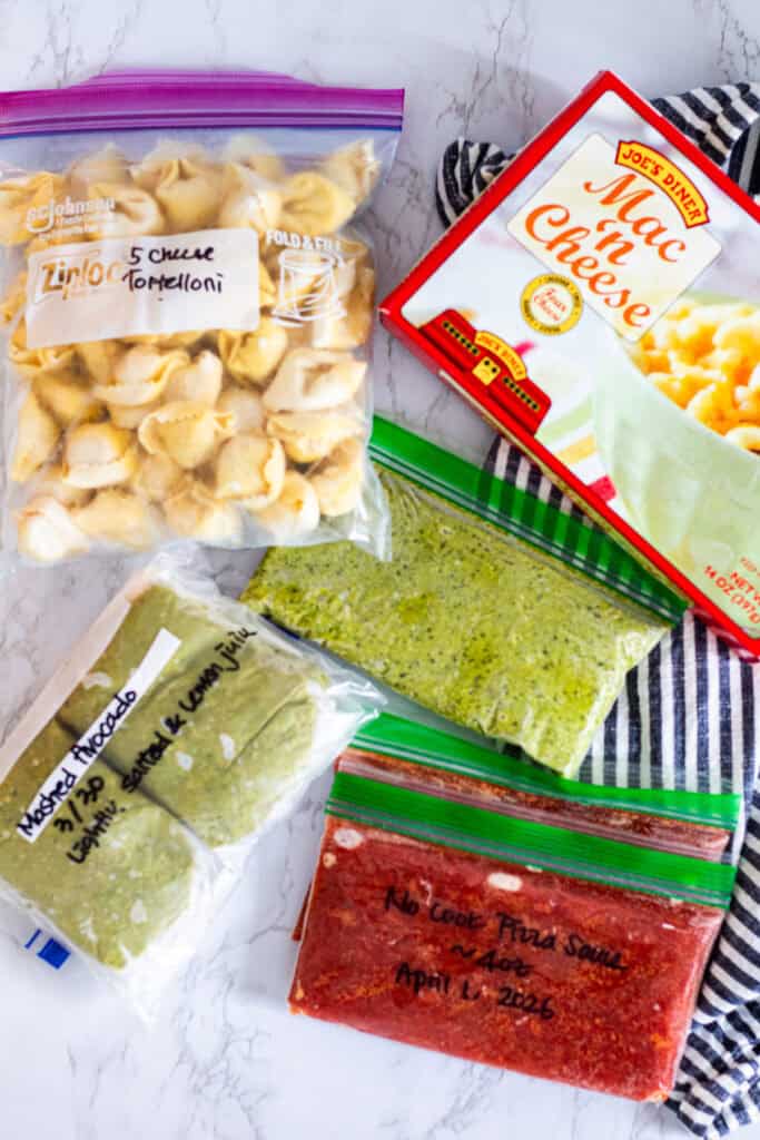 Frozen pesto, pizza sauce, tortellini, mac and cheese, and avocado stored in portions for a flexible meal planning system for two