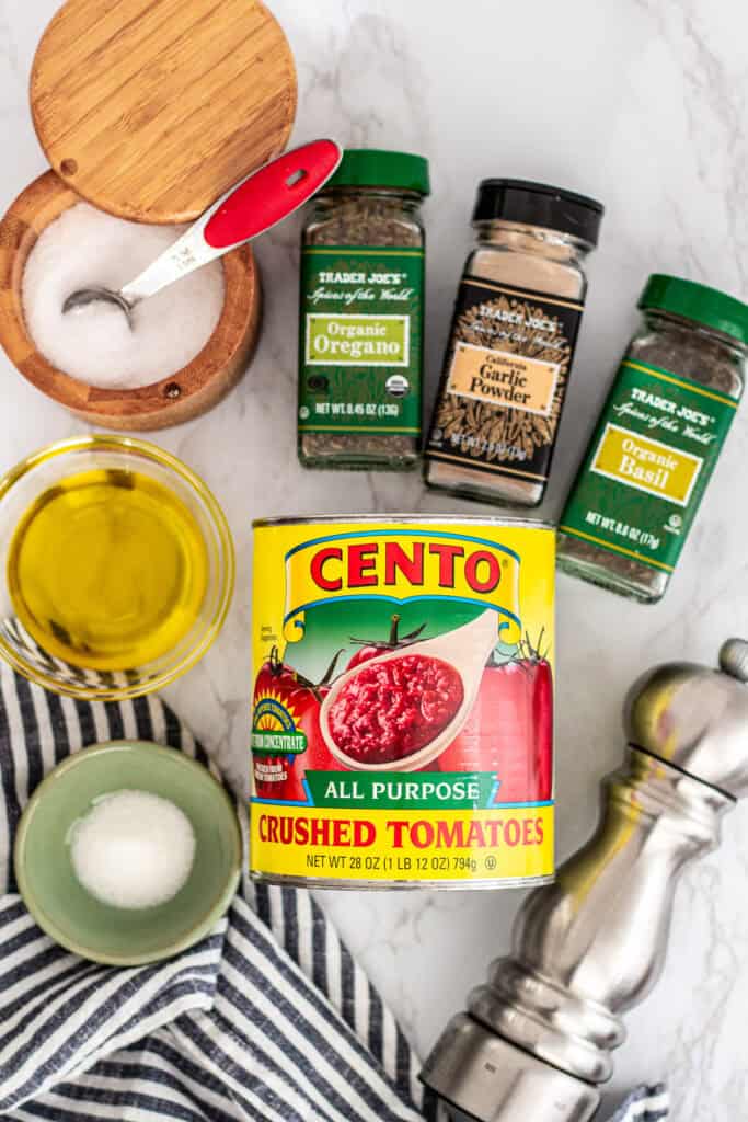 Ingredients for homemade no cook pizza sauce including crushed tomatoes, dried oregano, basil, garlic powder, olive oil, and salt