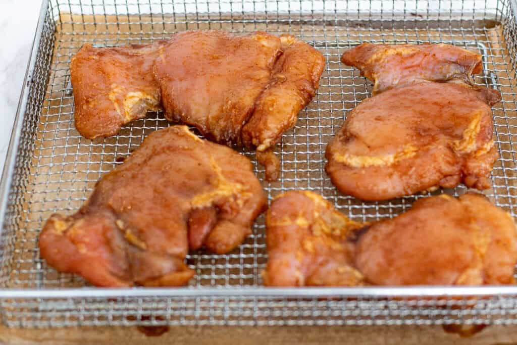 seasoned chicken thighs arranged in a single layer in the air fryer basket