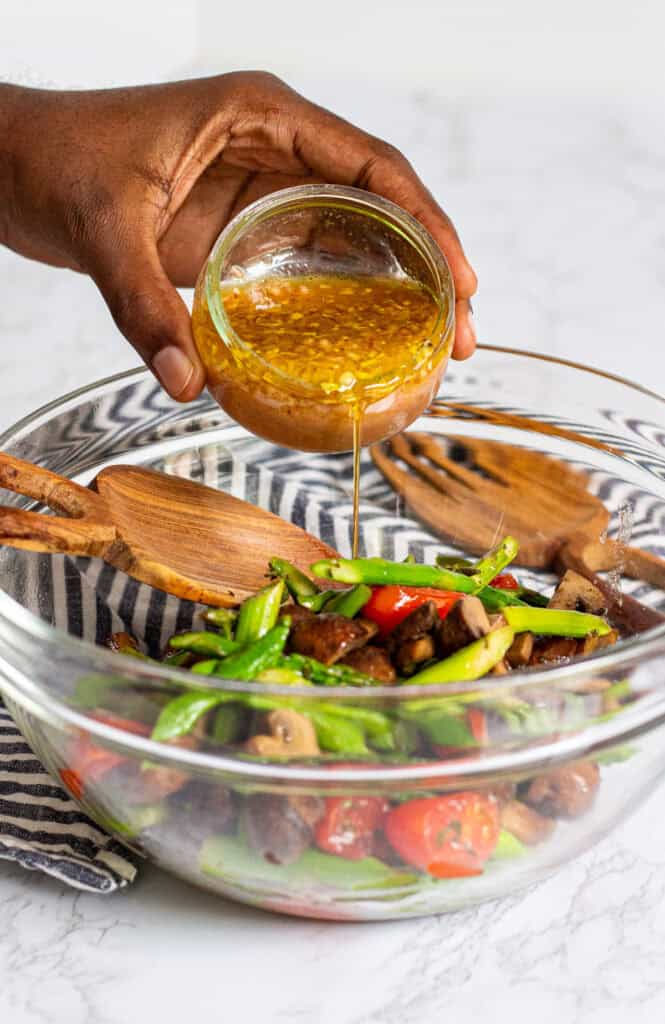 Pouring sweet and tangy vinaigrette over roasted asparagus, mushrooms, and tomatoes