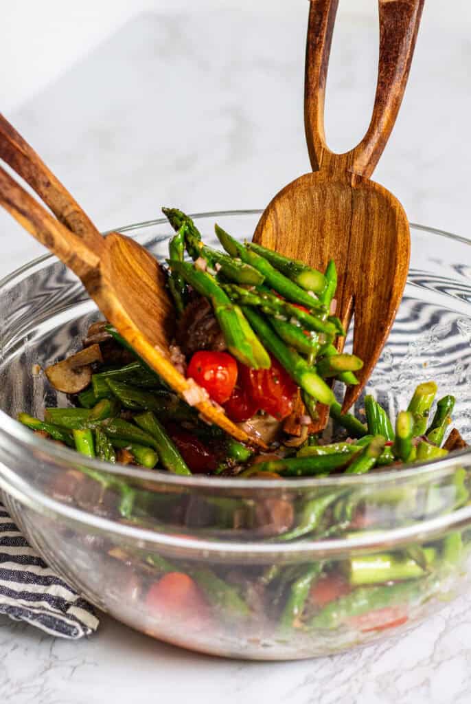 Tossing roasted asparagus salad with mushrooms and tomatoes in vinaigrette