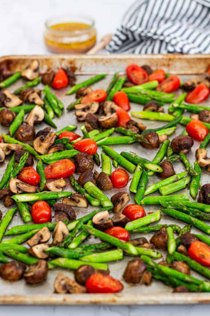 Asparagus, mushrooms, and cherry tomatoes spread on a sheet pan before roasting