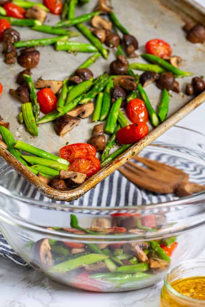Roasted asparagus, mushrooms, and tomatoes being transferred into a mixing bowl