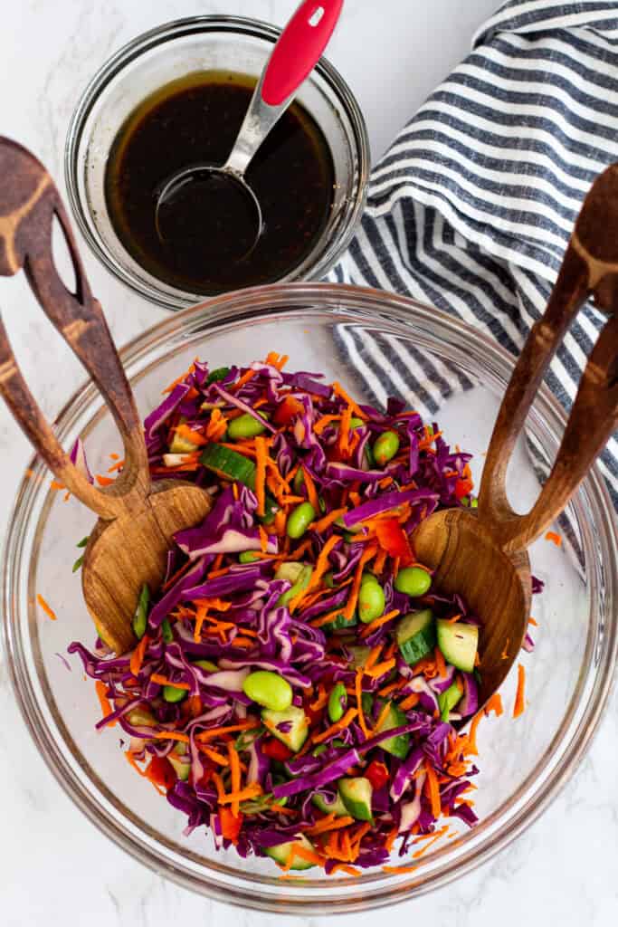 Shredded cabbage and carrots tossed with vegetables in a bowl with soy sesame dressing on the side