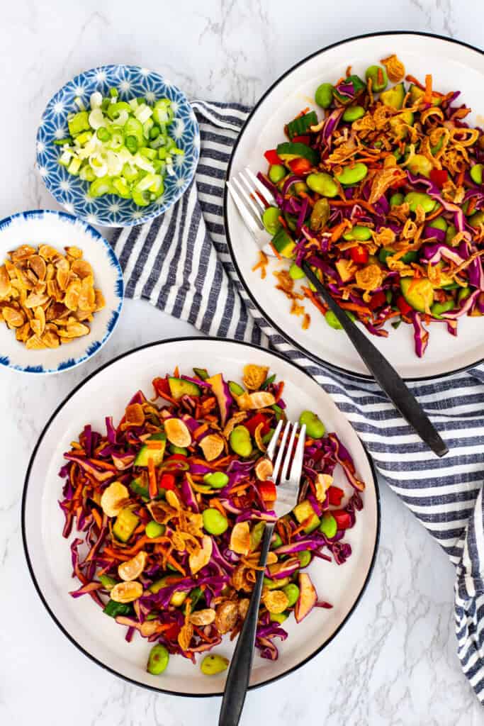 Cabbage carrot salad with soy sesame dressing served in bowls with crunchy toppings