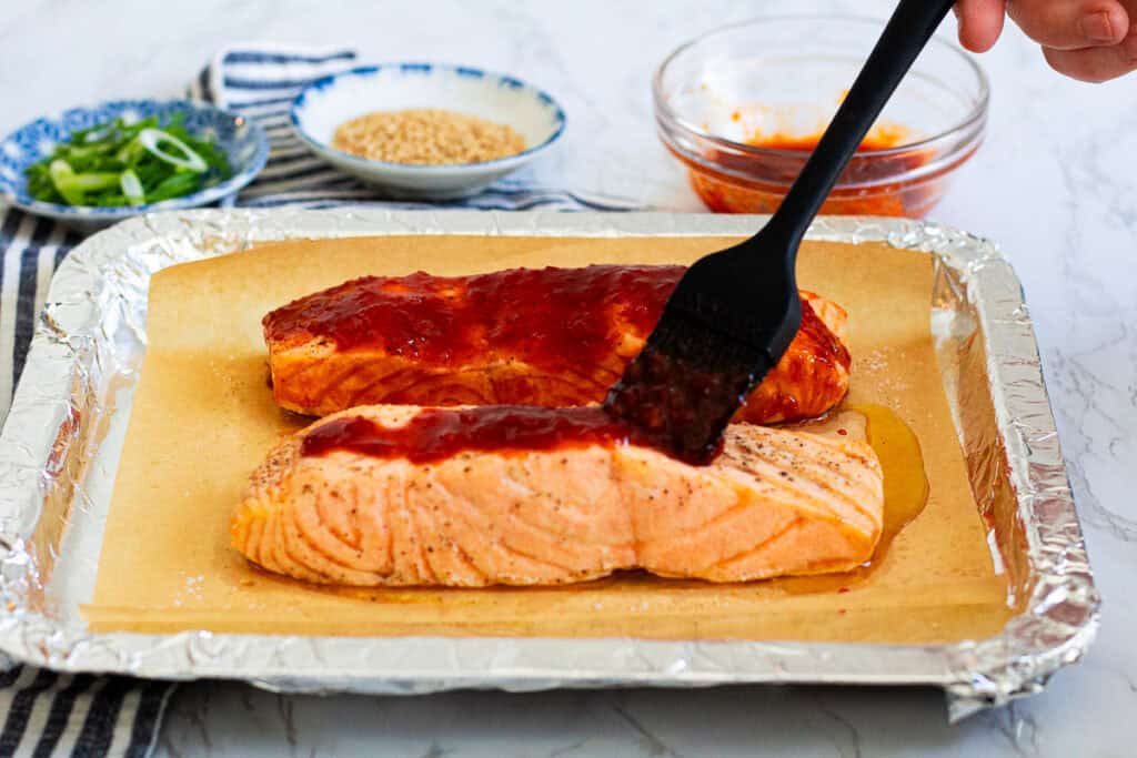 brushing sweet and spicy glaze over partially baked salmon before broiling