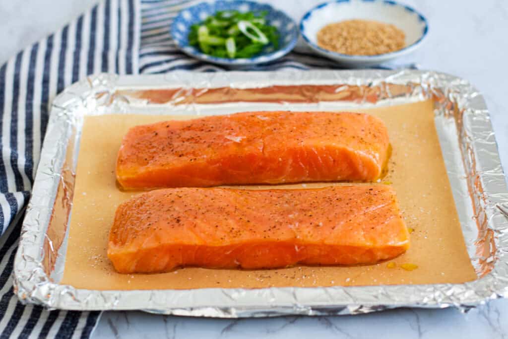 salmon fillets seasoned with salt and pepper on a parchment lined baking sheet