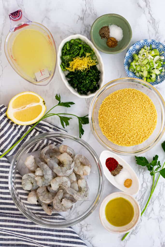 Ingredients for shrimp and couscous including raw shrimp, couscous, herbs, lemon, and spices