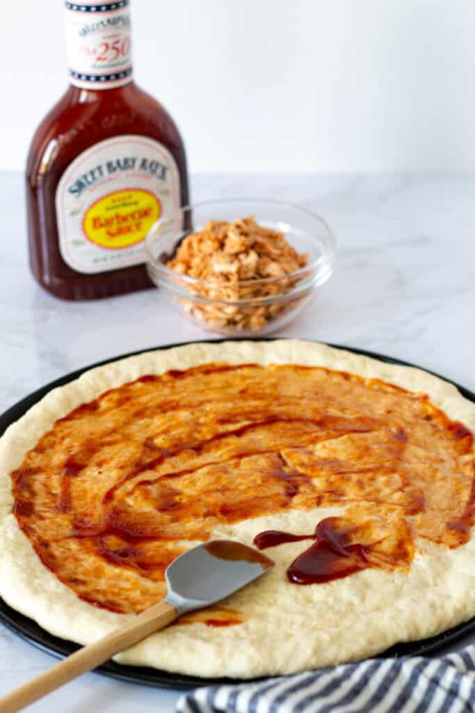 Pizza dough spread with BBQ sauce before adding the toppings.