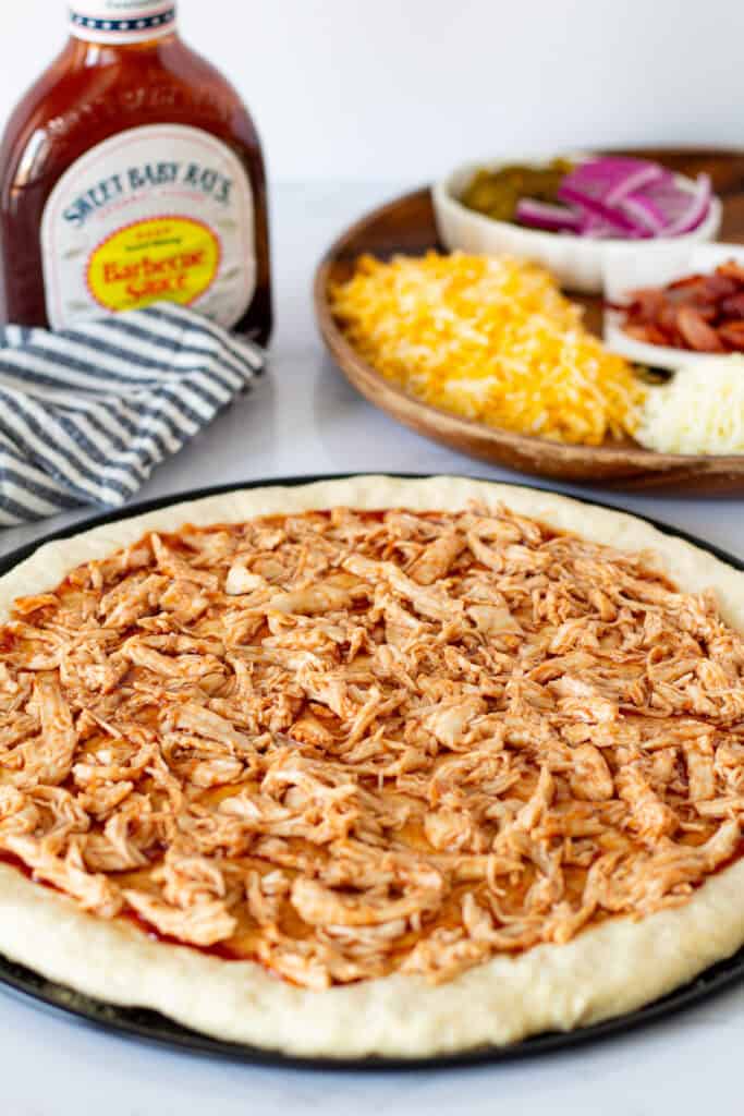 BBQ chicken evenly spread over the pizza dough before adding the remaining toppings.