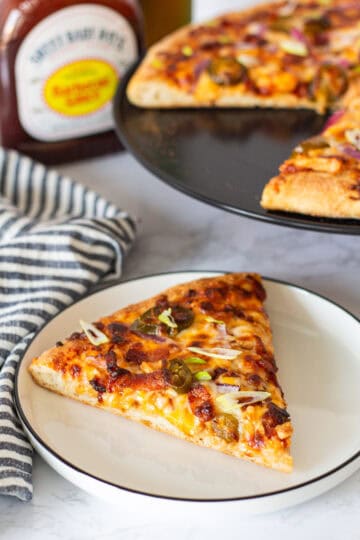 A slice of BBQ chicken and bacon pizza with crispy bacon, pickled jalapeños, red onion, and melted cheese.