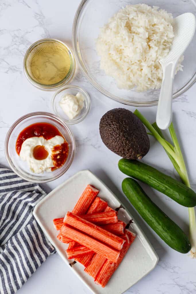 Ingredients for a California Roll Bowl including sushi rice, imitation crab, avocado, Persian cucumbers, green onion, sushi vinegar, mayonnaise, and spicy mayo.