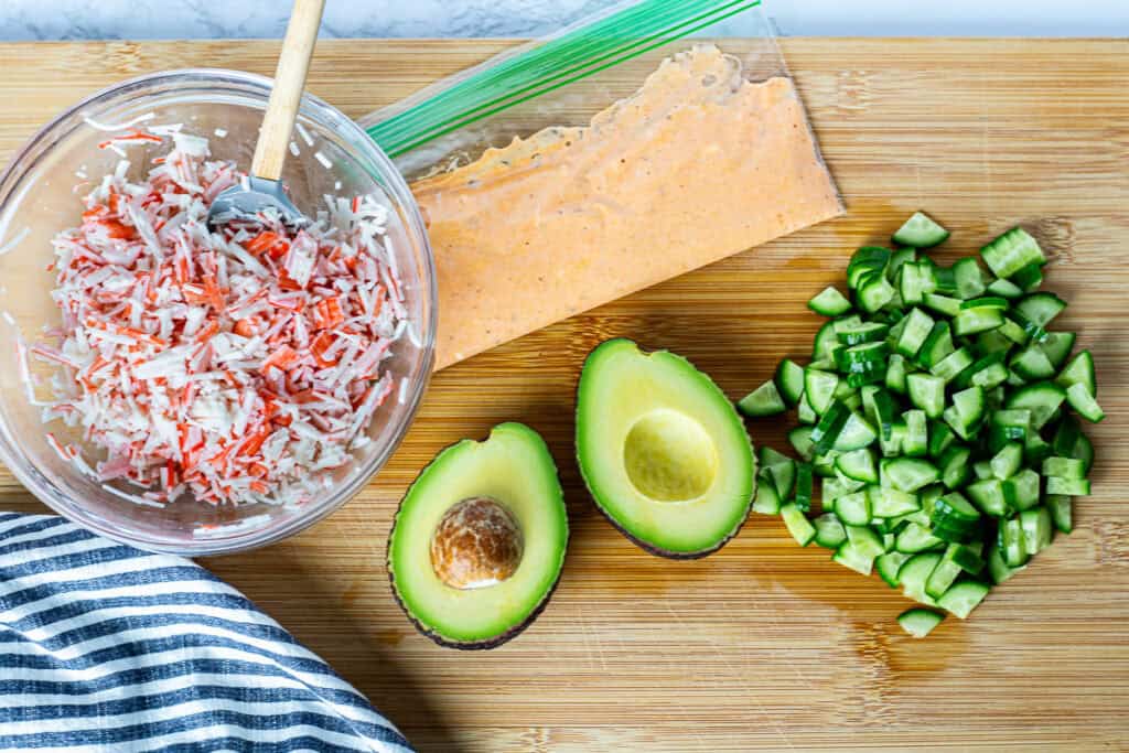 Chopped imitation crab, diced cucumber, avocado, and homemade spicy mayo prepared for assembling a California Roll Bowl.
