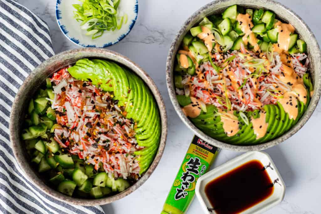 Two California Roll Bowls topped with imitation crab, avocado, cucumber, spicy mayo, and furikake, served with soy sauce and wasabi.