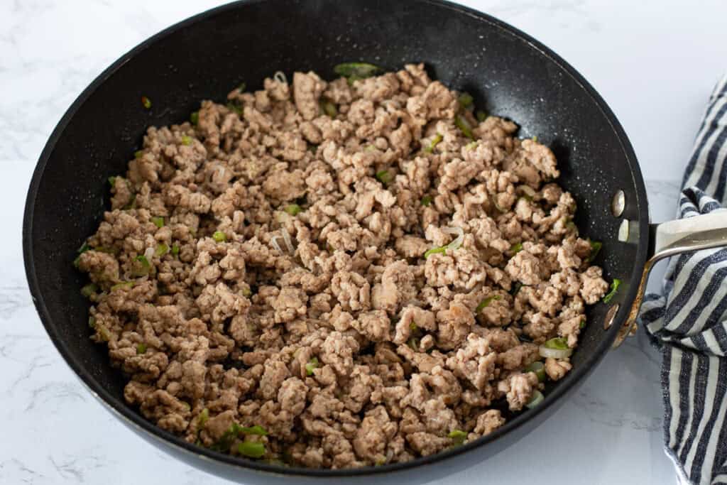Ground pork cooking with green onions and sugar in a skillet before adding the sauce.