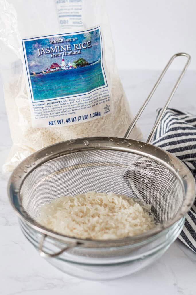 Rinsing jasmine rice in a fine mesh strainer under cold water