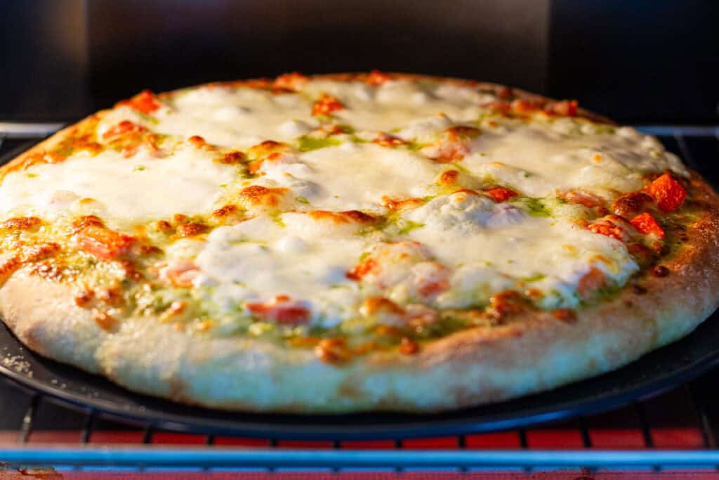 Pesto tomato pizza baking in the oven until the crust is golden and the cheese is melted and bubbly.