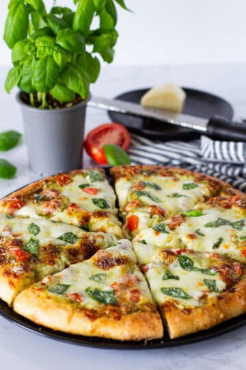 Whole homemade pesto tomato pizza topped with melted mozzarella, diced tomatoes, fresh basil, and Parmesan.