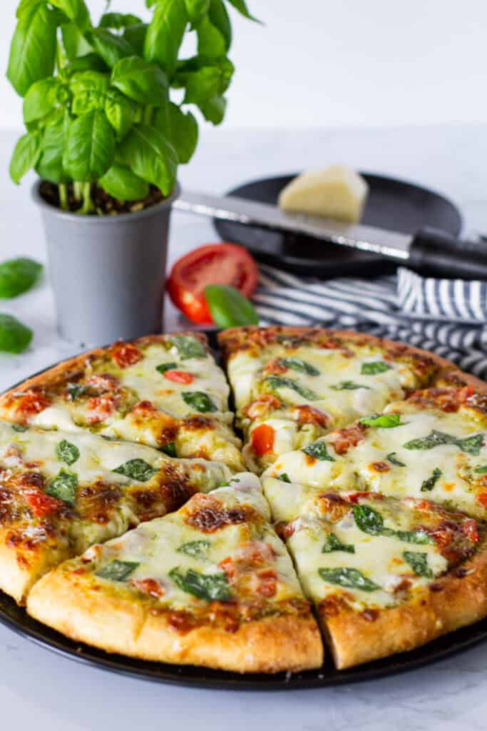 Whole homemade pesto tomato pizza topped with melted mozzarella, diced tomatoes, fresh basil, and Parmesan.