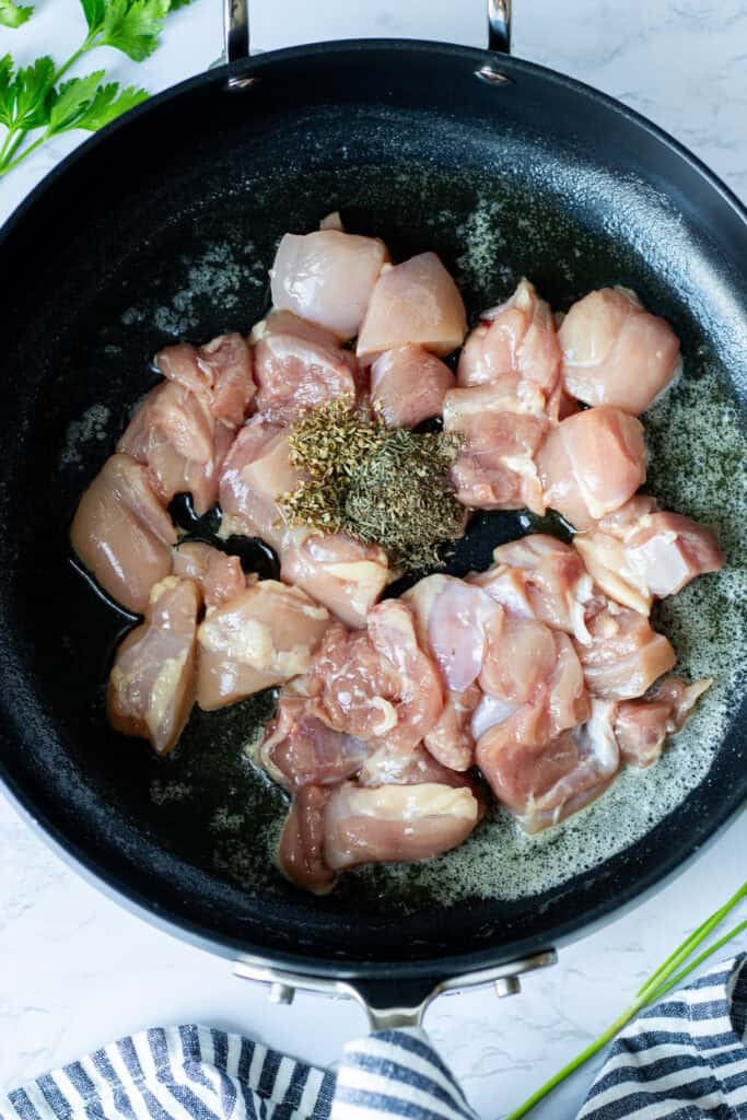 Bite-sized chicken thighs seasoned with dried herbs cooking in a sauté pan