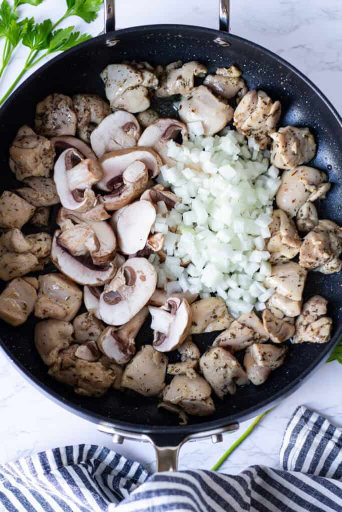 Sliced baby bella mushrooms and chopped onion added to seasoned chicken in a sauté pan