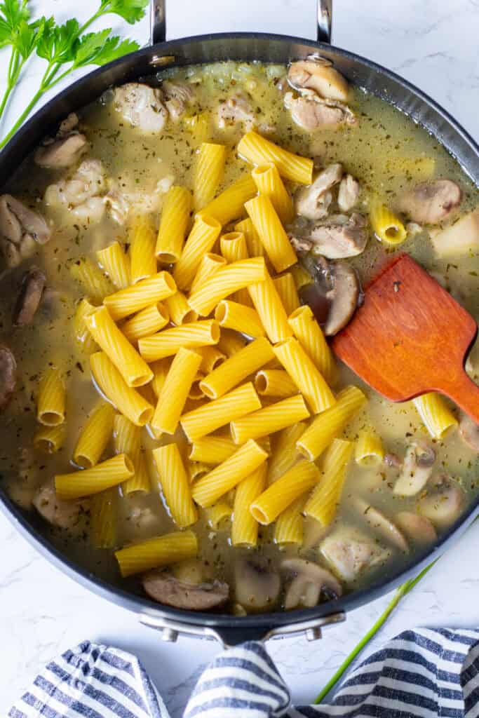 Rigatoni cooking with chicken and mushrooms in chicken broth in a sauté pan