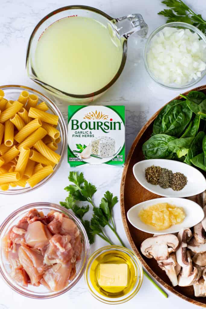 Ingredients for Boursin chicken pasta including chicken thighs, rigatoni, Boursin cheese, mushrooms, spinach, onion, garlic, and chicken broth