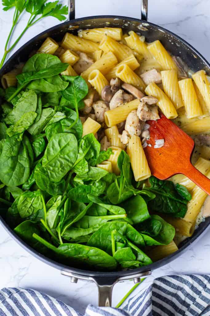 Fresh baby spinach added to creamy Boursin chicken pasta in the pan