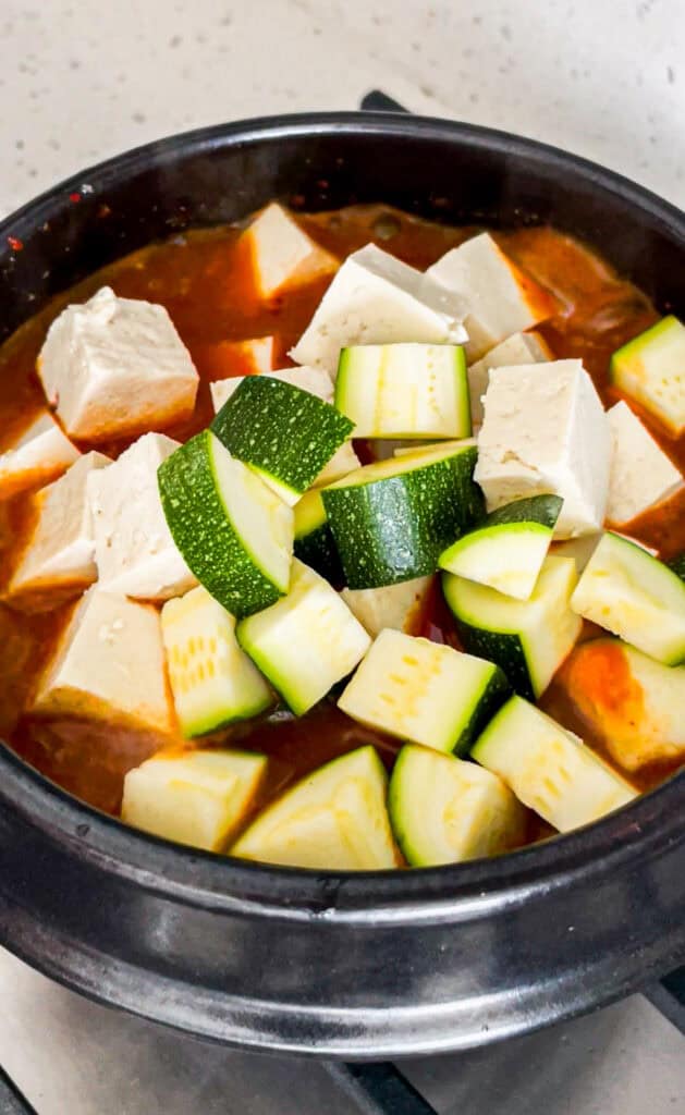 Diced zucchini and tofu added to the red gochujang stew