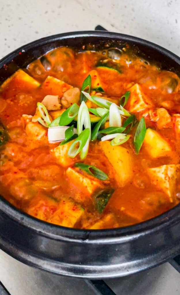 Bubbling gochujang jjigae with chicken, tofu, potato, zucchini, and sliced green onion