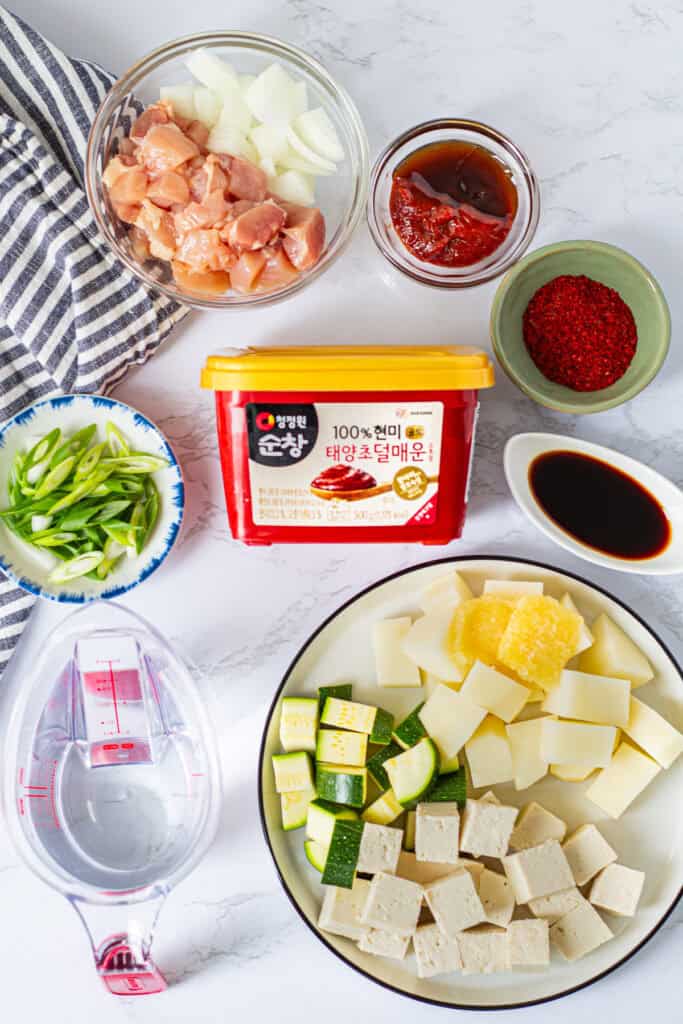 Ingredients for gochujang jjigae with chicken, including gochujang, gochugaru, tofu, potato, zucchini, and aromatics