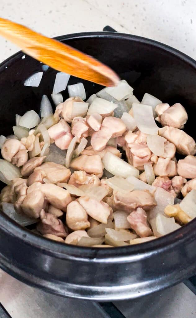 Diced chicken thigh and onion cooking in a small Korean clay pot