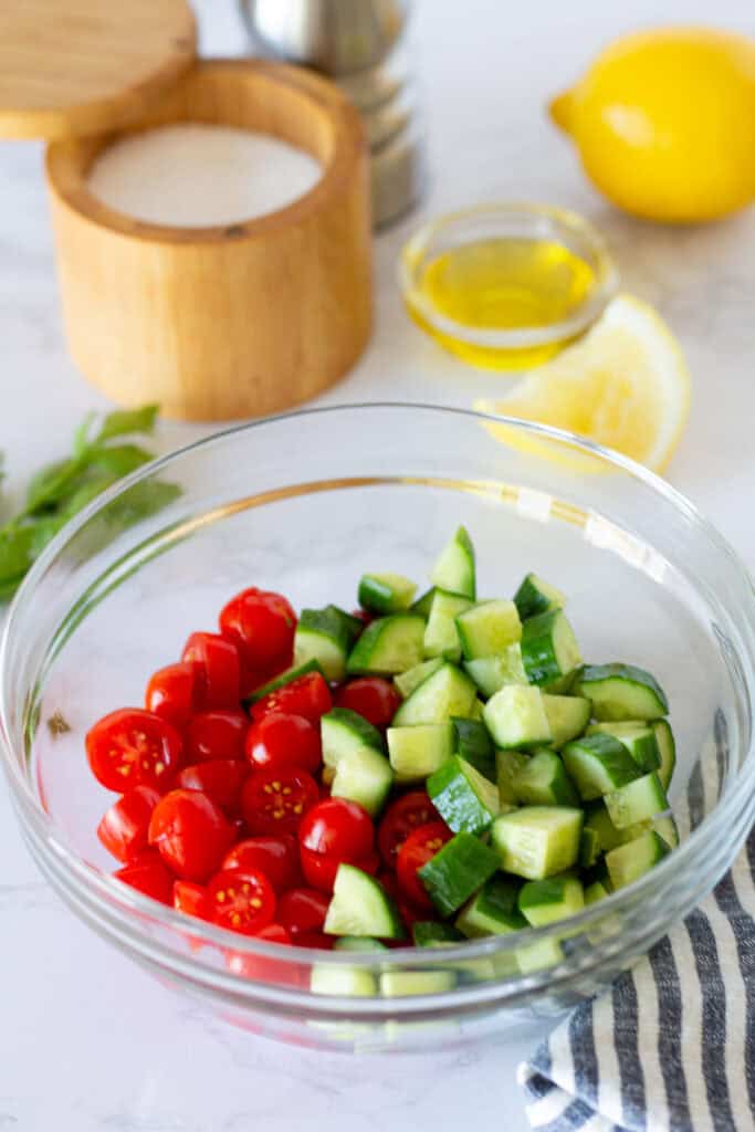 Cherry tomatoes and diced cucumber in a bowl before being mixed into a fresh cucumber tomato salad for Greek turkey bowls.