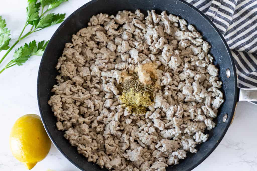 Ground turkey topped with garlic, oregano, onion powder, and lemon pepper seasoning before being mixed together.
