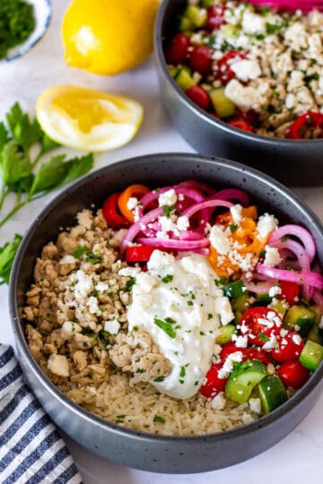 Two Greek turkey bowls with garlic basmati rice, seasoned ground turkey, cucumber tomato salad, tzatziki, feta, and pickled onions.