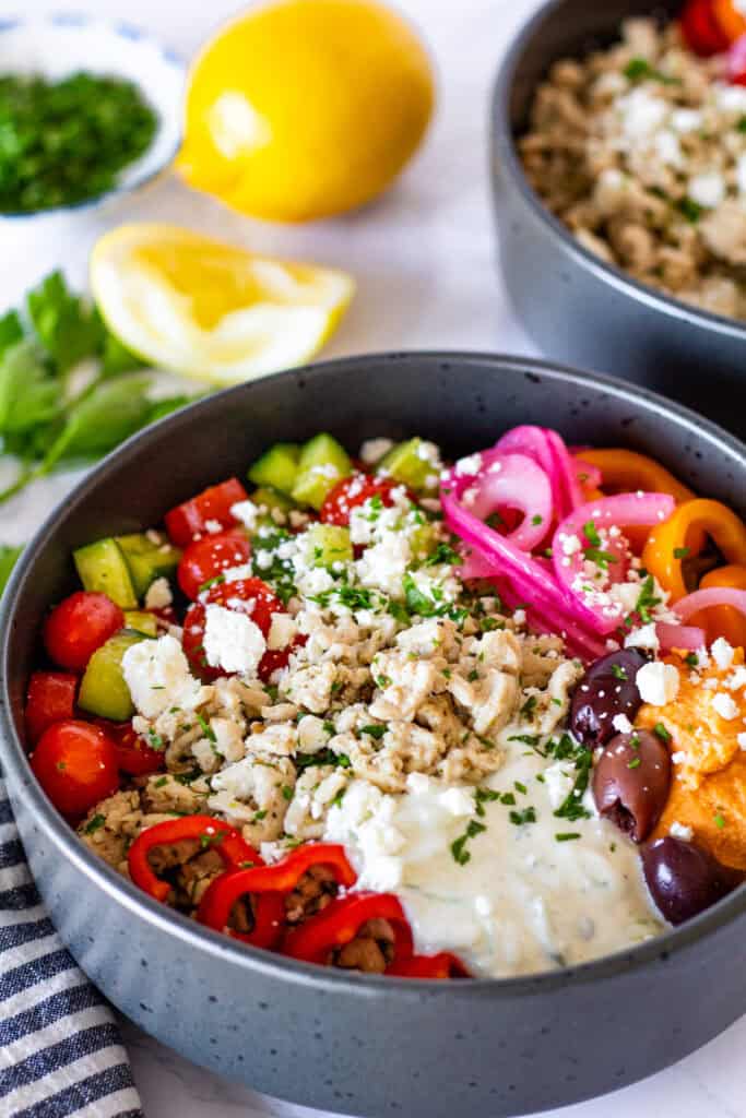 Greek turkey bowl with garlic basmati rice, seasoned ground turkey, cucumber tomato salad, tzatziki, feta, olives, hummus, and fresh vegetables.