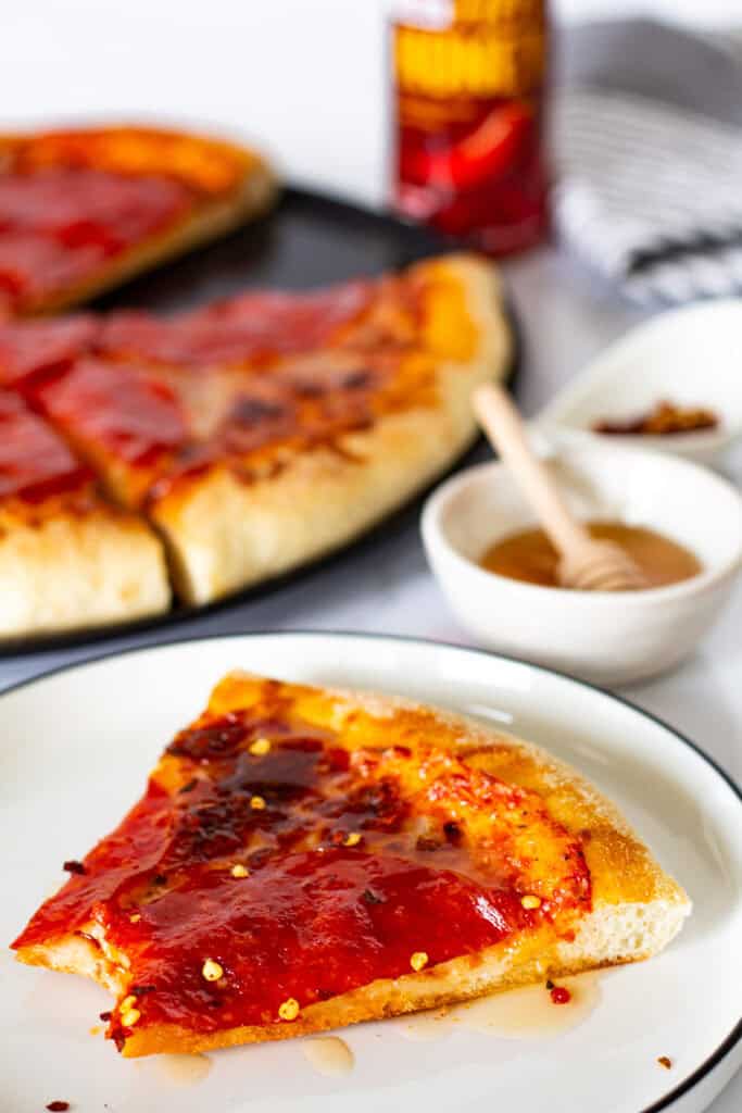 Slice of pepperoni pizza drizzled with hot honey and topped with red pepper flakes