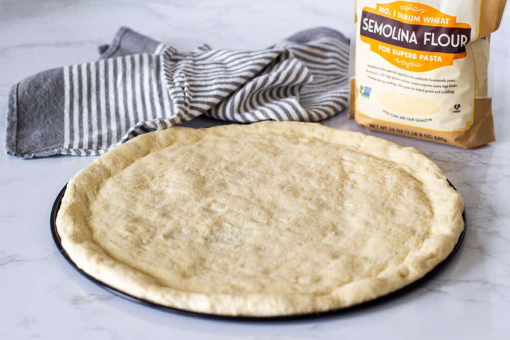 Pizza dough stretched on a round pizza pan with semolina flour