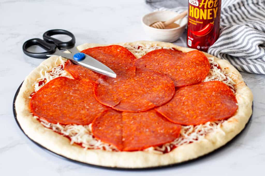 Large deli-style pepperoni slices arranged over mozzarella cheese on pizza dough